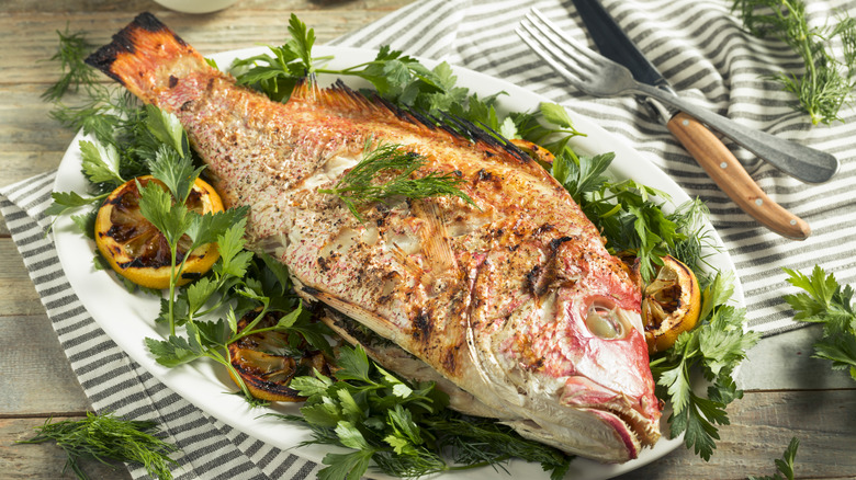 A whole grilled fish plated on a bed of greens with lemon.
