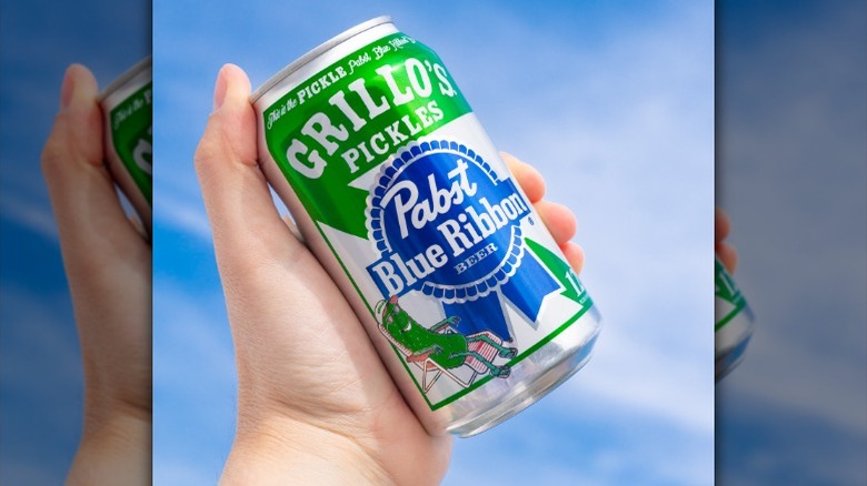hand holding a can of Grillo's Pickles Pabst Blue Ribbon beer against a blue sky