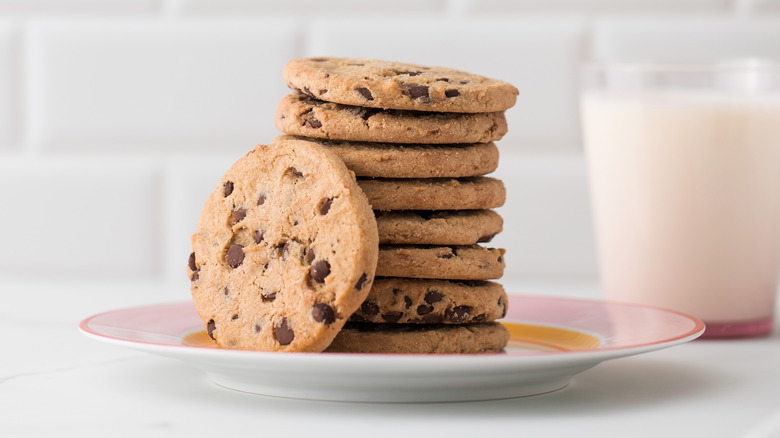 Stacked chocolate chip cookies on a white plate by a glass of milk