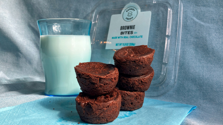 Two stacks of round brownie bites stand slightly precariously in front of a glass of milk and the lid of the brownie container.