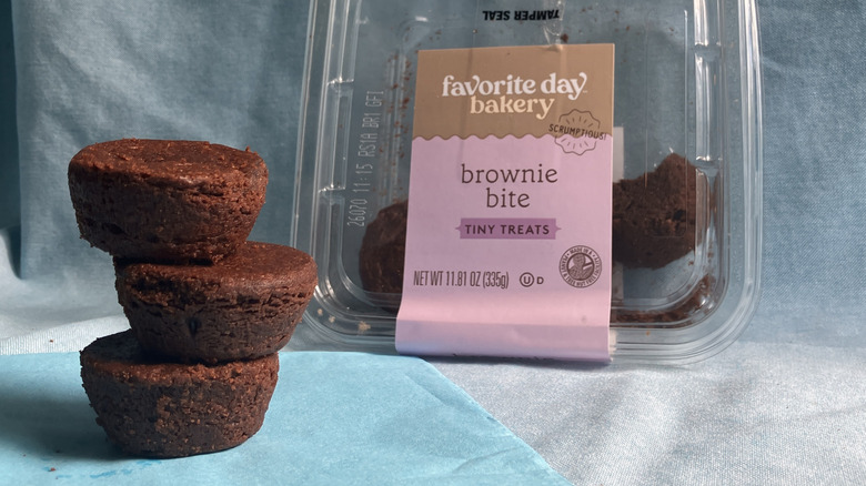 Stack of round brownie bites next to plastic container of Favorite Day Bakery brand brownie bites.