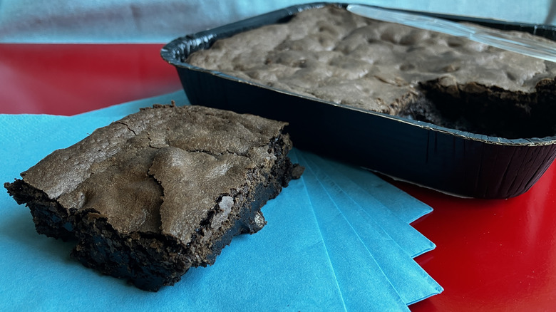 A single slice from a pan of brownies sits beside the pan on a blue napkin.