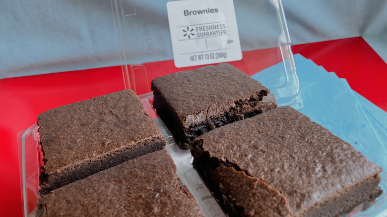 Four large brownie squares on red and blue table with brownie container lid seen in the background.