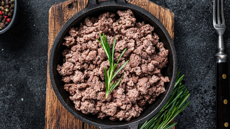 Top view of cooked ground beef with fresh rosemary garnish in cast iron pan