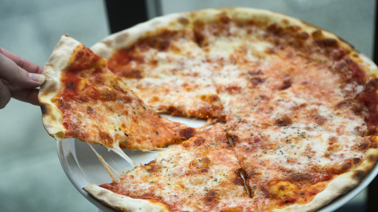 A person pulls a slice from a whole New York style pizza