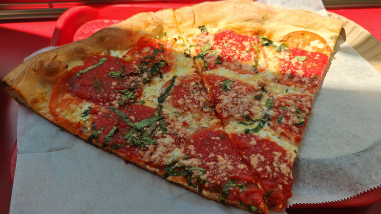 Thin crust pepperoni NYC style pizza with shredded basil and cheese on a paper plate and a red tray