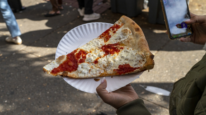 A person caries a New York slice pizza walking along the sidewalk