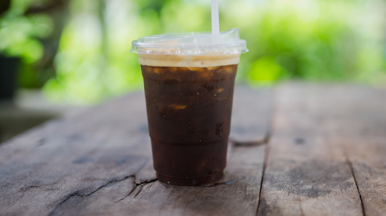 An iced coffee in a plastic cup on a wooden table outside