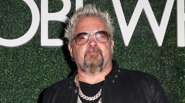 Guy Fieri wearing a black jacket and sunglasses at an event.