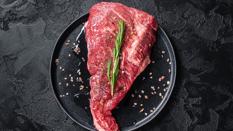 A raw tri-tip steak sitting on a black plate.