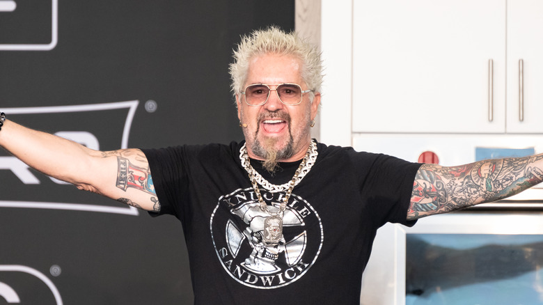 Guy Fieri in a black shirt with arms spread wide