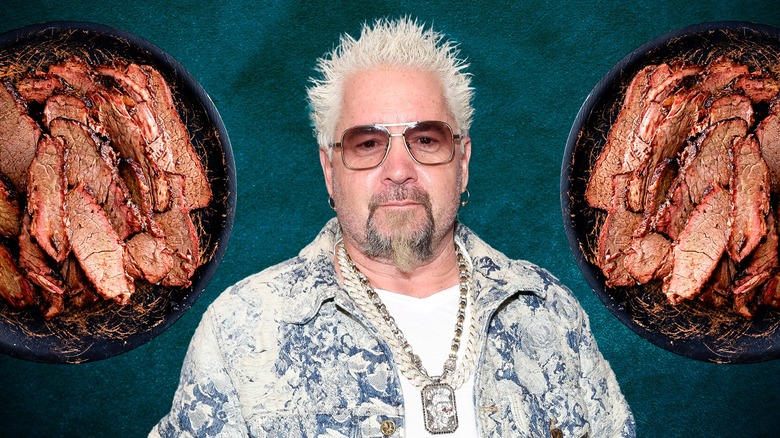 Guy Fieri wearing sunglasses, necklace, bleach blonde hair and surrounded by two plates of brisket