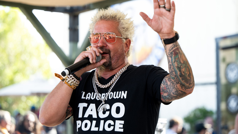 Guy Fieri waving his hand while speaking into a microphone