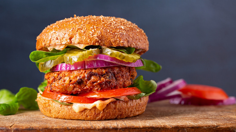 Vegan burger with bun, sauce, lettuce, tomato, red onion and a saucy-looking patty