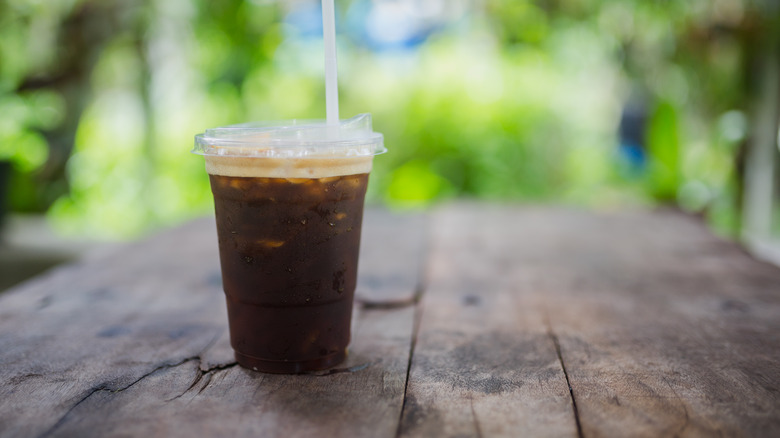 An iced coffee in a plastic cup on a wooden table outside