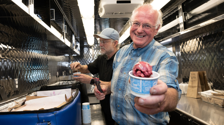 Jerry Greenfield holding a cup of ice cream and Ben Cohen scooping ice cream
