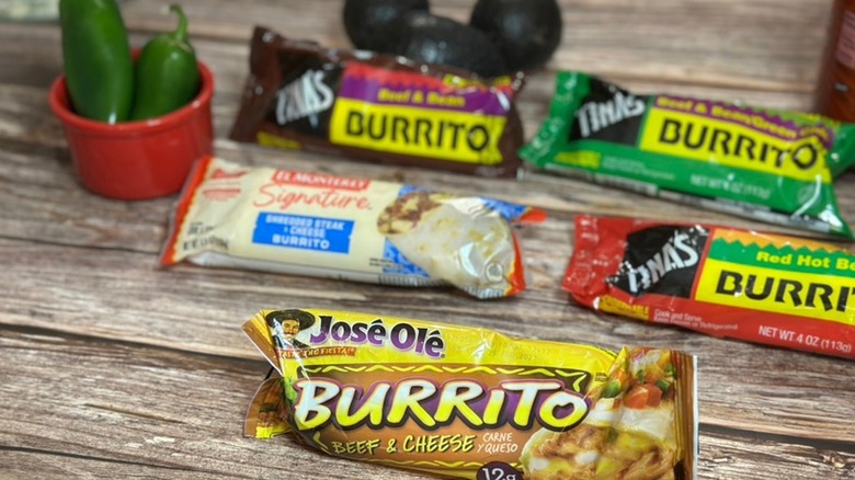 Five different frozen beef burritos sitting in their packaging on a table near some jalapenos.