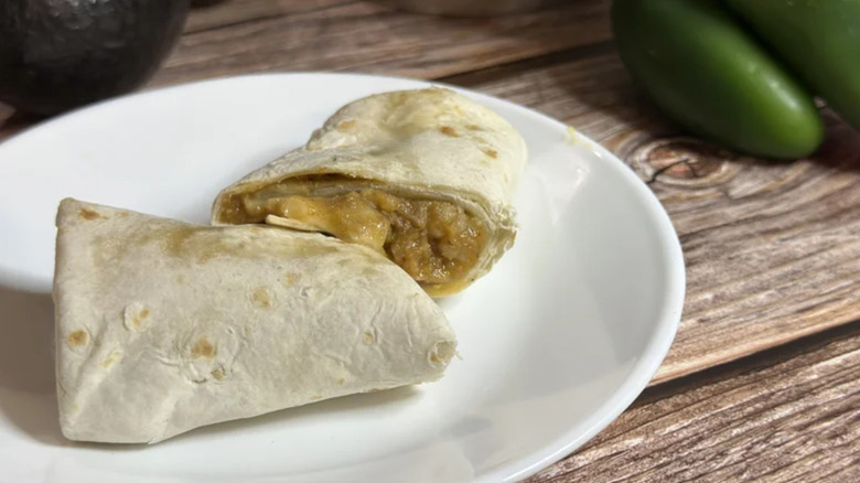 El Monterey beef burrito sitting on a small plate next to jalapenos on a table.