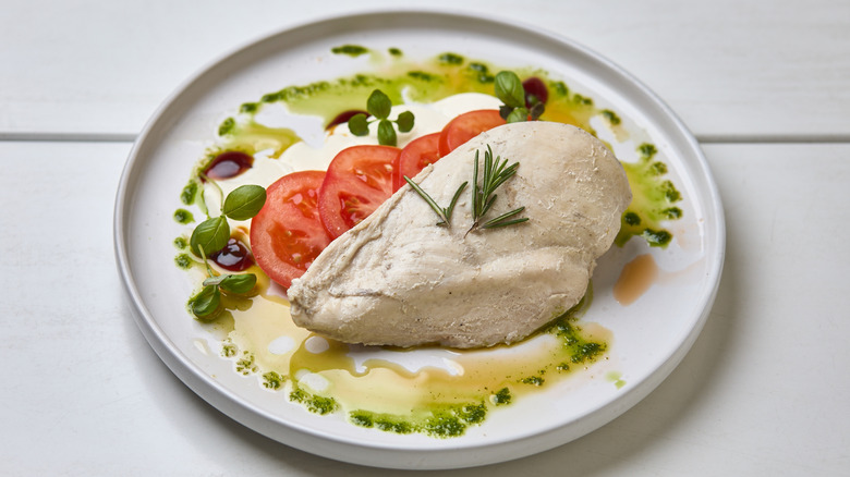 Poached chicken breast on plate with tomato and herbs