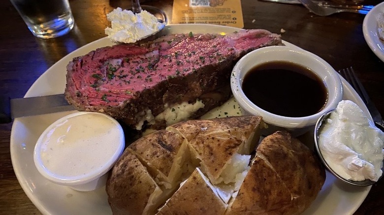 A thick cut of pink prime rib served with baked potato at Bull and Bush restaurant.