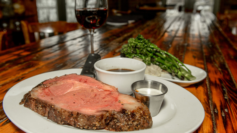 Tender prime rib on restaurant plate with side of au jus, vegetables, and glass of red wine