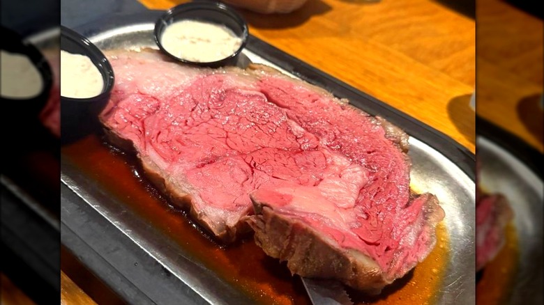 Prime rib served in a metal tray of au jus with condiment cups of horseradish.