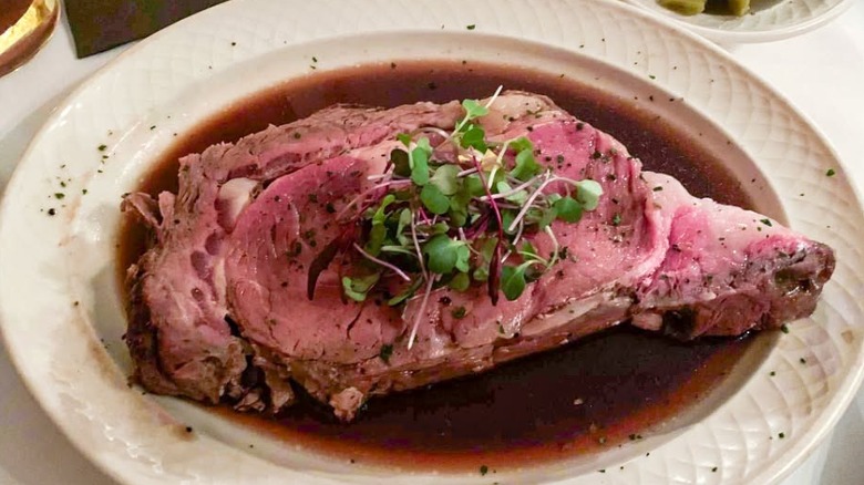 Succulent prime rib served on a white plate in a pool of rich au jus and topped with microgreens at The Merrick Inn Restaurant