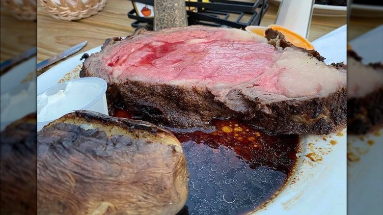 Thick cut, pink prime rib steak and charred baked potato in a plate of au jus at Trail's End Steakhouse