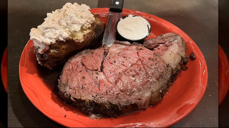 A plate of Crazy Horse Steak House prime rib and loaded baked potato on plate.