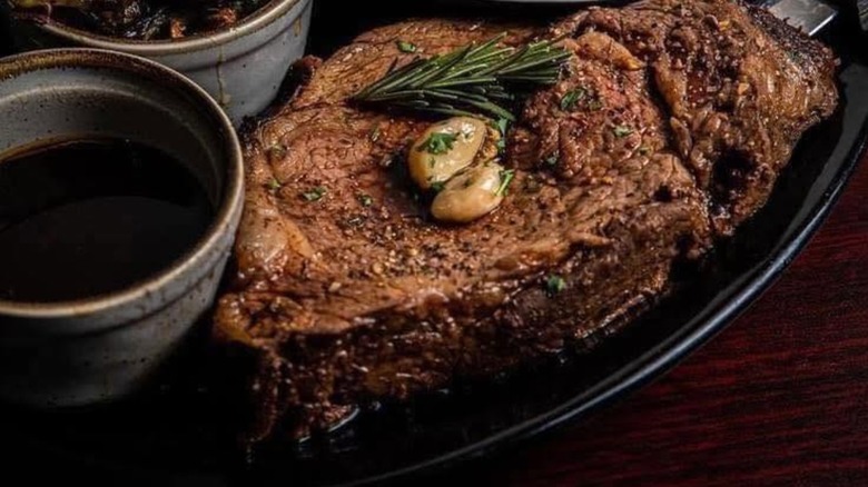 A prime rib topped with garlic and seasonings alongside a dish of au jus at Benson's Steakhouse and Taproom.
