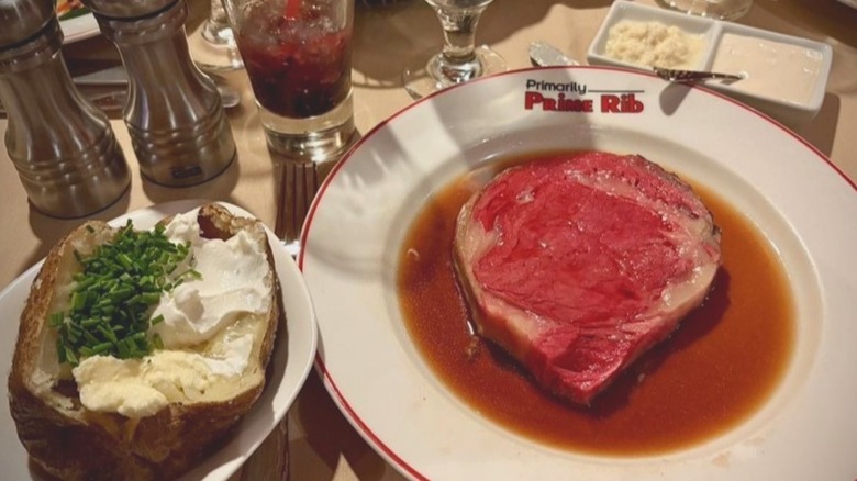 A baked potato sits next to a plate of deep-red prime rib resting in a pool of au jus at Primarily Prime Rib restaurant.