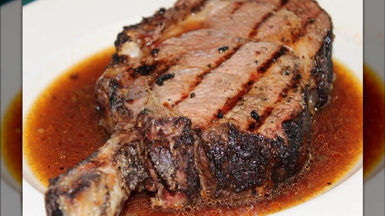 A cut of Fremont Pizzeria's massive chargrilled bone-in prime rib soaks in a puddle of au jus on plate.