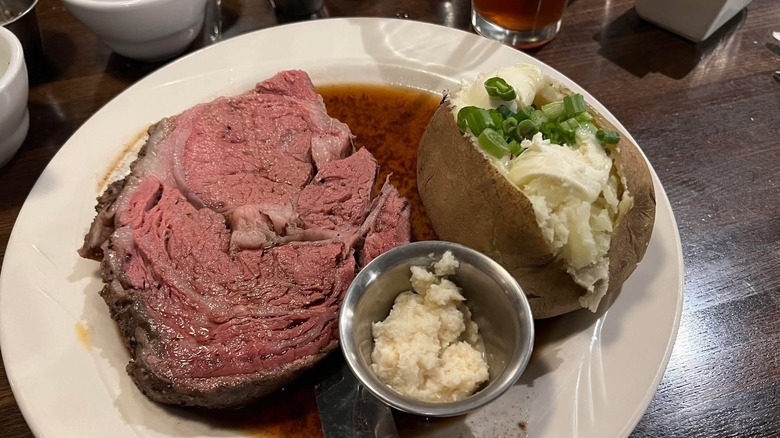 A rosy prime rib steak served at Albuquerque Pelican's Restaurant with a loaded baked potato in a pool of rich au jus.