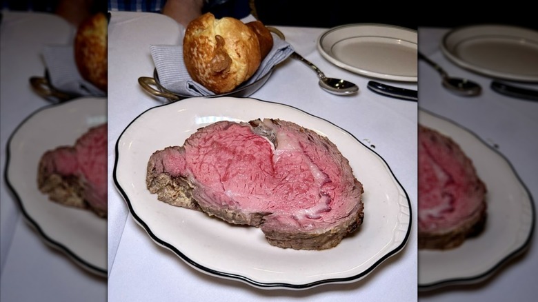 The Rib Room's King's Cut House Prime Rib served on plate with Yorkshire pudding on white cloth table.