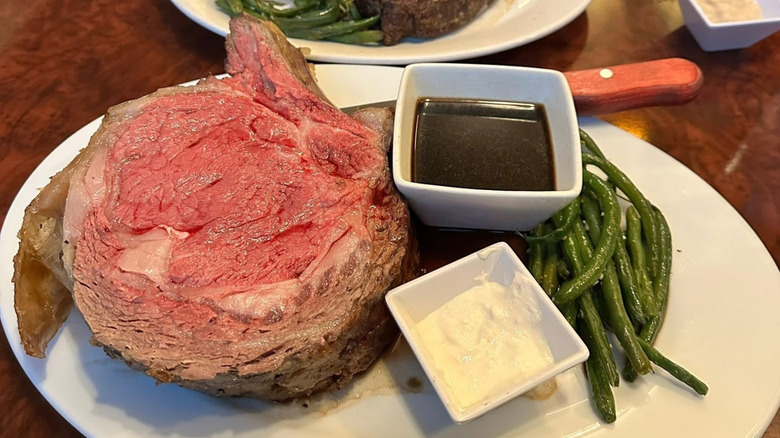 A nearly 40 ounce cut of bone-in prime rib takes up most of the plate at Legends Steakhouse with sides of sauce and green beans.