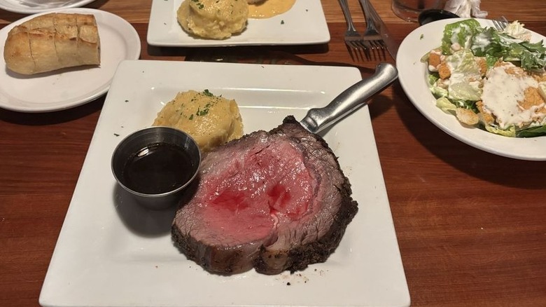 Prime rib dinner at The Barrel Steak and Seafood House served with au jus, mashed potatoes, bread, and salad on plates.