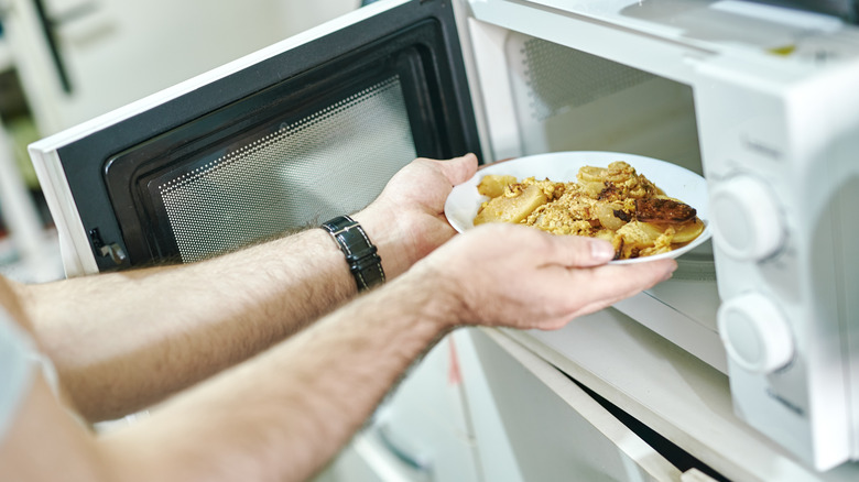 A man heating up leftovers in a microwave