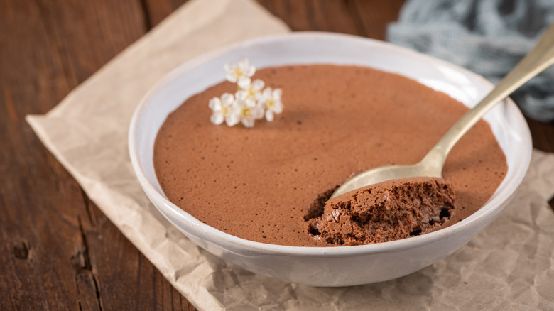 A bowl of chocolate pudding with a spoon in it and small white flowers