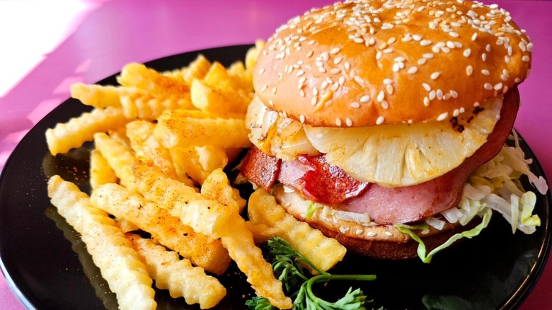 A close-up of a Hawaiian burger with fries at The Purple Onion Deli & Grill