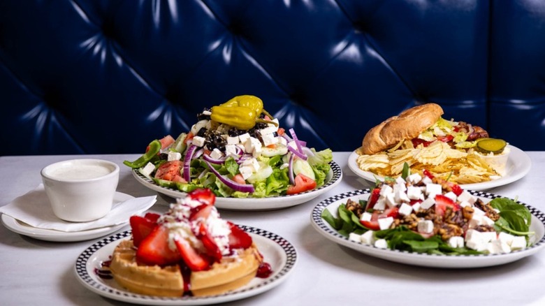 A table at Honey Bee Diner with plates of Belgian waffle, salads, and a burger with chips