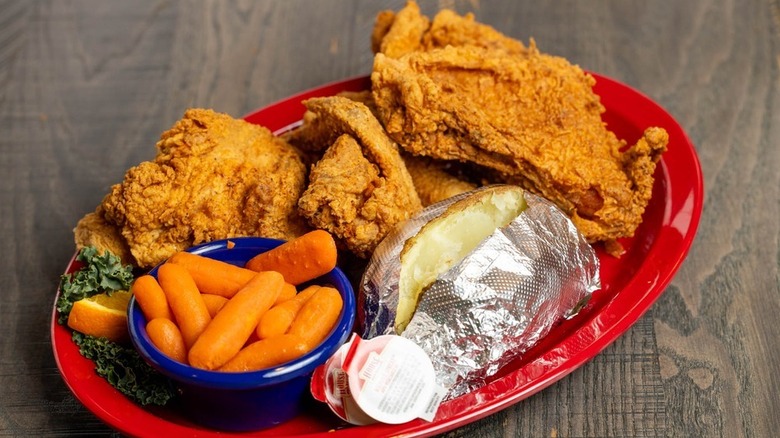 A plate of fried chicken served with a baked potato and side of baby carrots at Gingham's Homestyle Restaurant