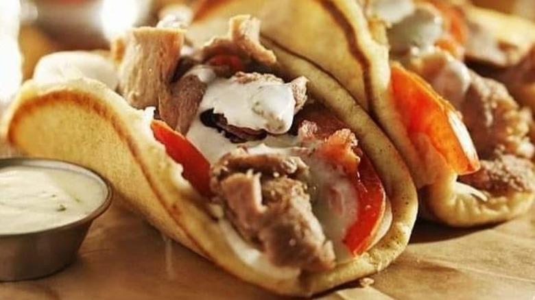 A close-up of gyro meat in pitas next to dipping sauce at Gyro Bites