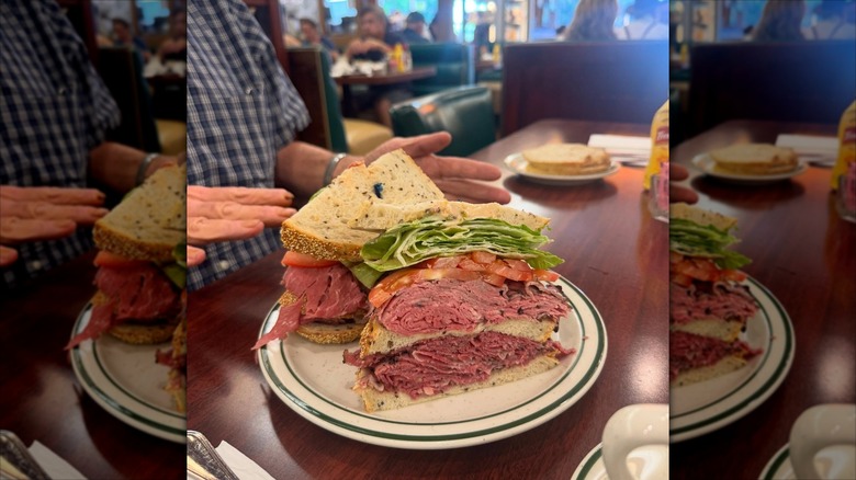 A sandwich sliced in half on a plate, stuffed high with beef, tomatoes, and lettuce