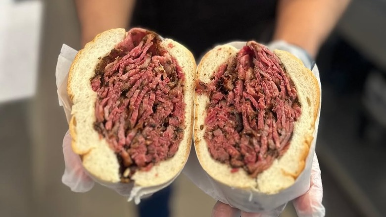 Hands holding up a pastrami sandwich, cut in half
