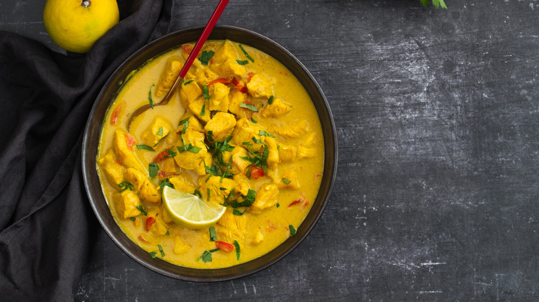 A bowl of yellow Thai curry in a black bowl sitting on a dark surface.