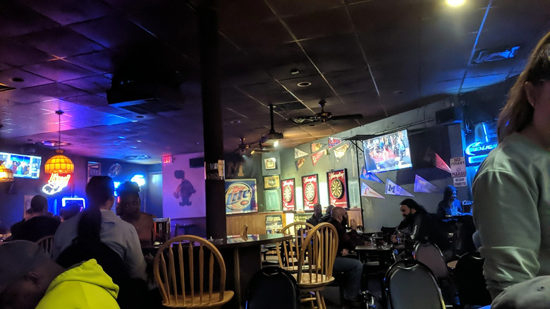 Interior shot of the inside of a dimly lit bar with low ceilings, dart boards, and a few patrons sitting around