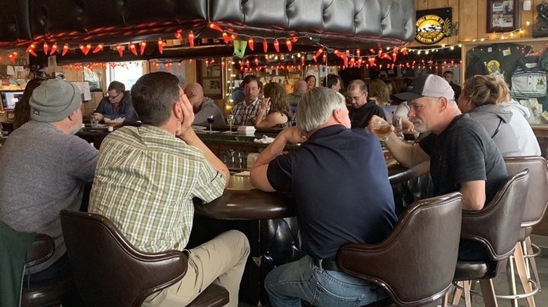 Interior of a rustic, rectangle-shaped bar with brown barstools occupied by middle-aged men