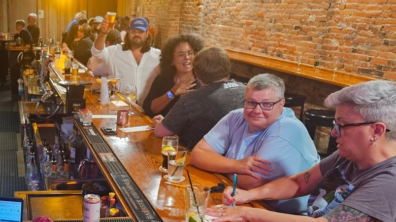 The interior of a long, wood bar with brown brick walls and happy-looking customers occupying every barstool while one smiles at the camera