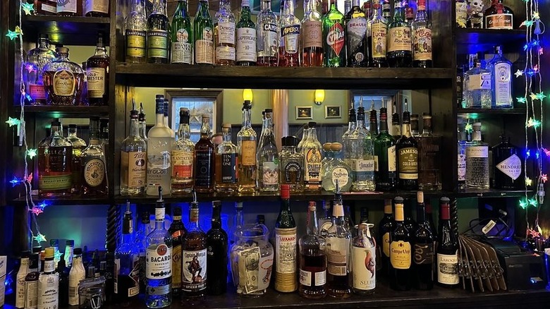 A multilevel barback lined with booze bottles in a dimly lit bar; star-shaped string purple, blue , and green string lights hang from each side