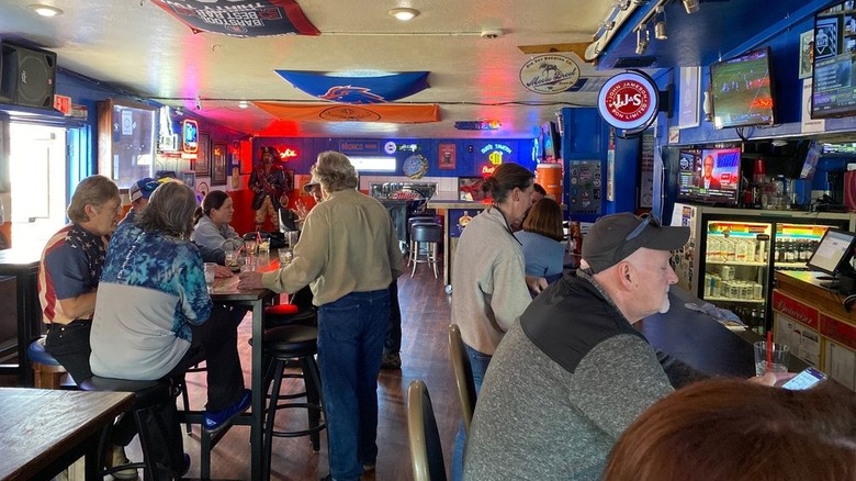 Interior of a blue and orange-themed bar with daylight coming in; people mingle around the tables while others sit at the bar